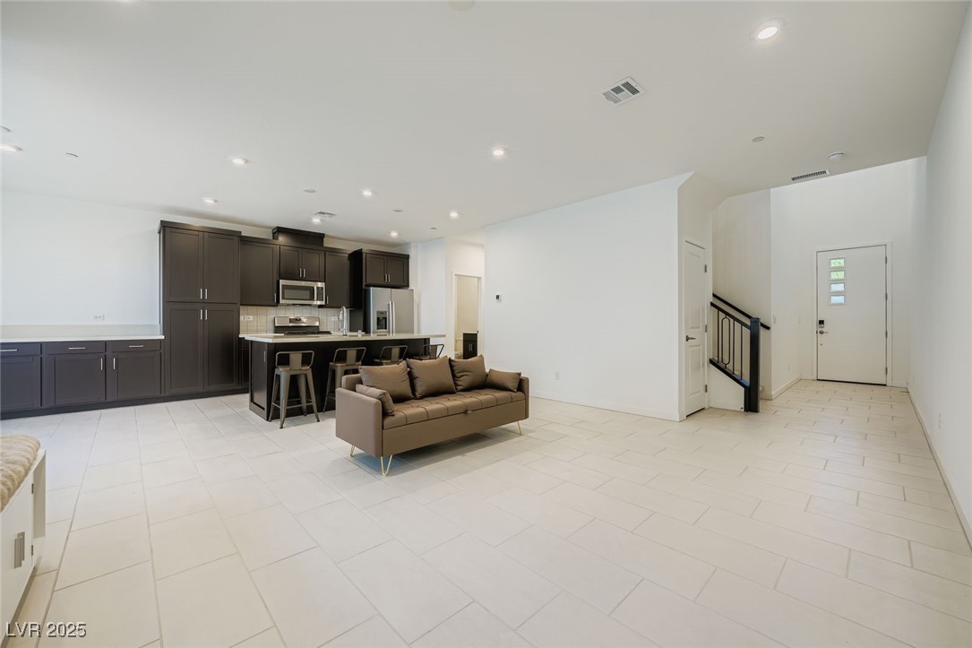 Open-plan kitchen and living area with dark cabinets, a white island, and a brown sofa.