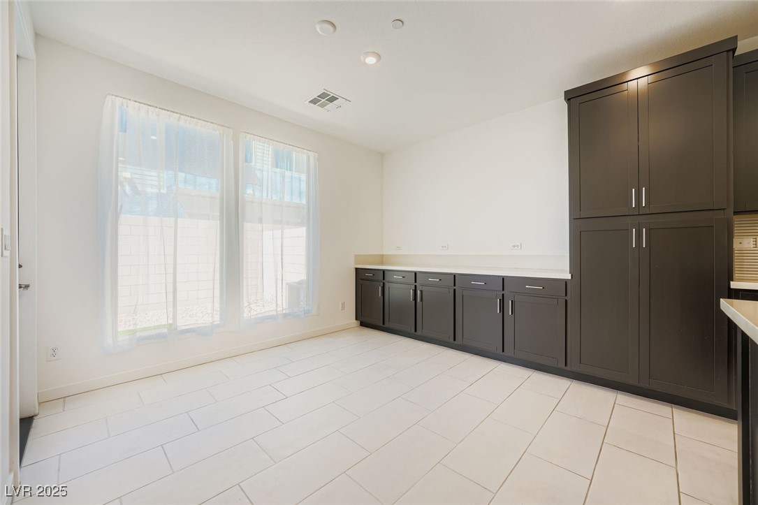 Unfurnished utility room with dark built-in cabinets, a long countertop, and two curtained windows.
