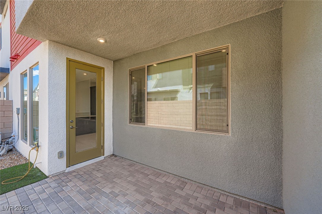 Covered patio entry with paver flooring, olive door, and wide window.