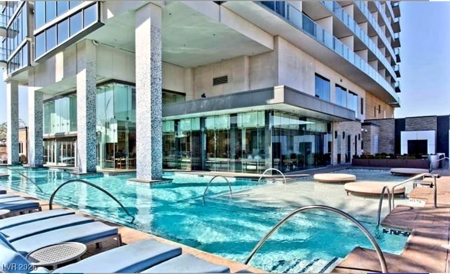 Condominium pool beside a glass-walled high-rise, with lounge chairs and curved metal rails.