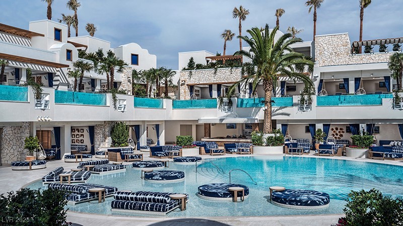 Outdoor pool with turquoise-edged balconies, palm trees, and cushioned lounge chairs.