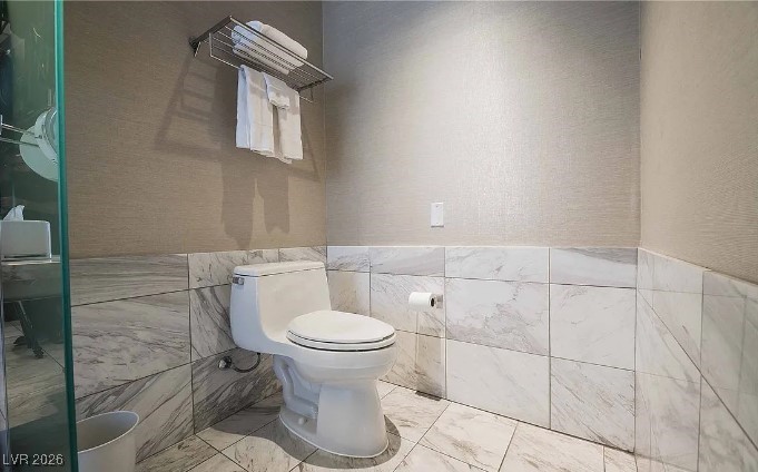 Modern bathroom with marble-patterned tile, a white toilet, and a glass shower enclosure.