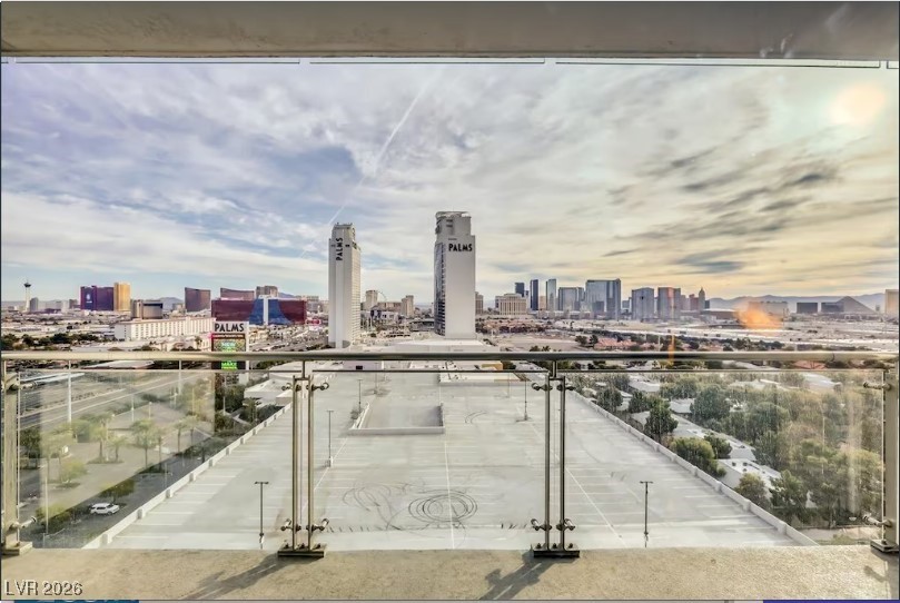 Las Vegas skyline and Palms towers viewed from a glass-railed balcony above a parking lot.