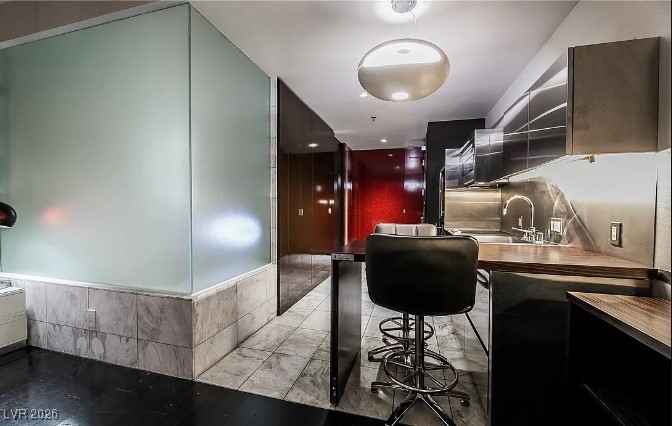 Modern condo kitchen with glossy dark cabinets, a stainless steel backsplash, and a black bar stool.
