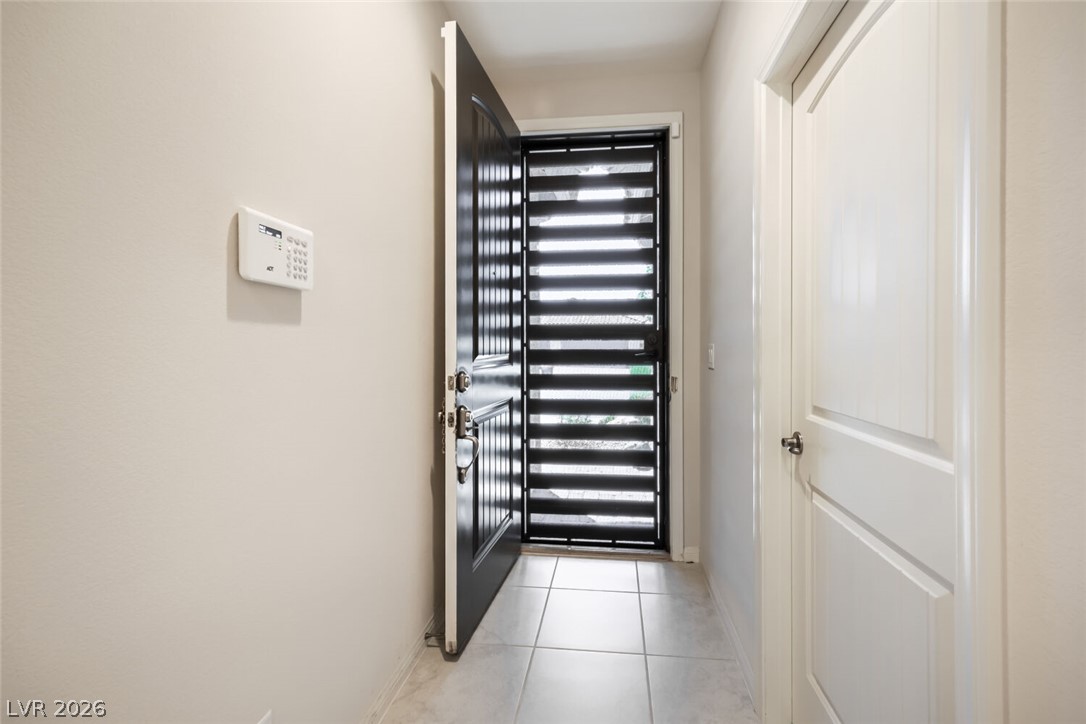 Entry hallway with tiled floor, open dark front door, and black horizontal-slat security door.