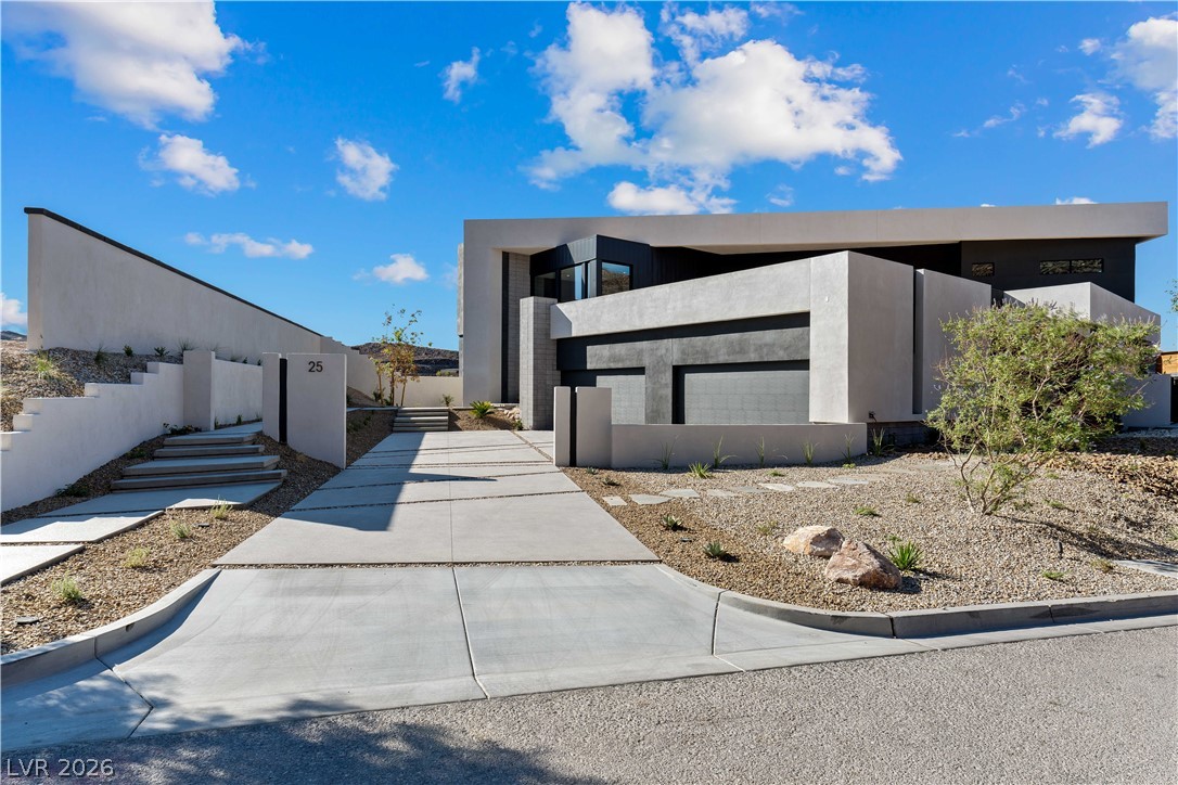 Modern concrete home with an angular facade, broad driveway, and desert landscaping.