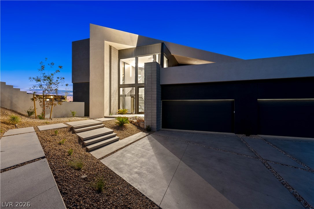 Modern Henderson home with a tall glass entry, dark garage doors, and desert landscaping at dusk.