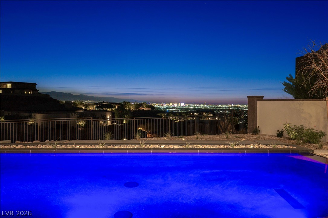 Backyard pool glowing blue at night, overlooking city lights and mountains.