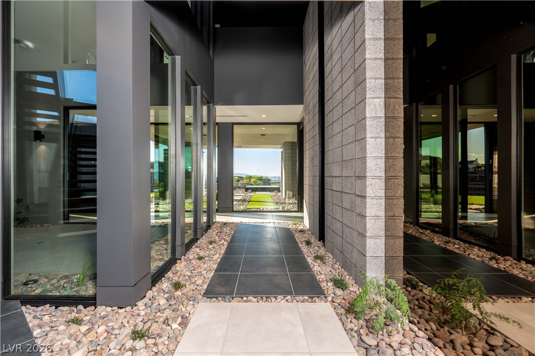 Modern home entrance with a tiled walkway, glass walls, block masonry, and rock landscaping.