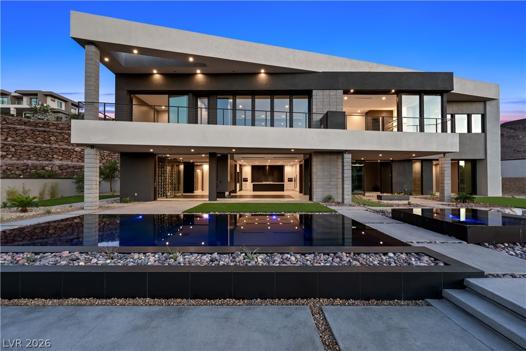 Modern two-story home with angular concrete facade and a reflecting pool at dusk.