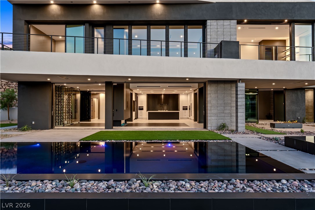 Modern two-story home with expansive glass doors and a reflecting pool at dusk.