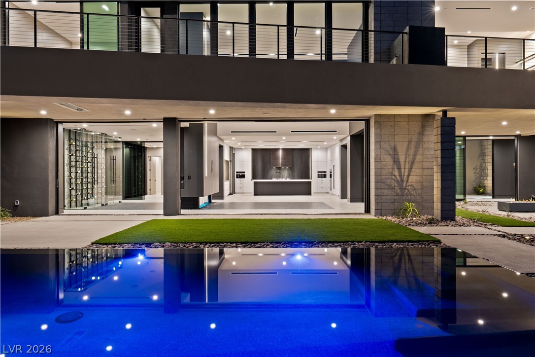 Modern two-story home with a glass-fronted kitchen opening onto an illuminated pool and lawn.