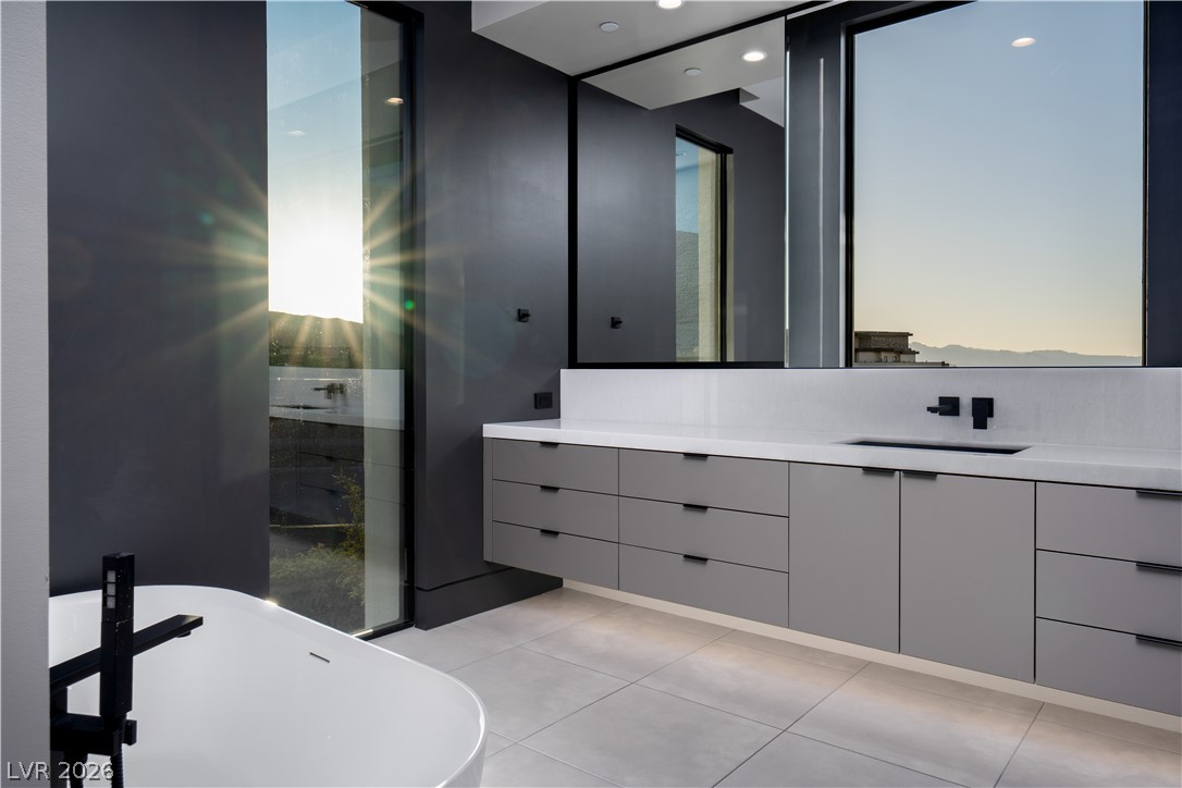 Modern bathroom with a floating gray vanity, freestanding tub, and large windows overlooking distant mountains.