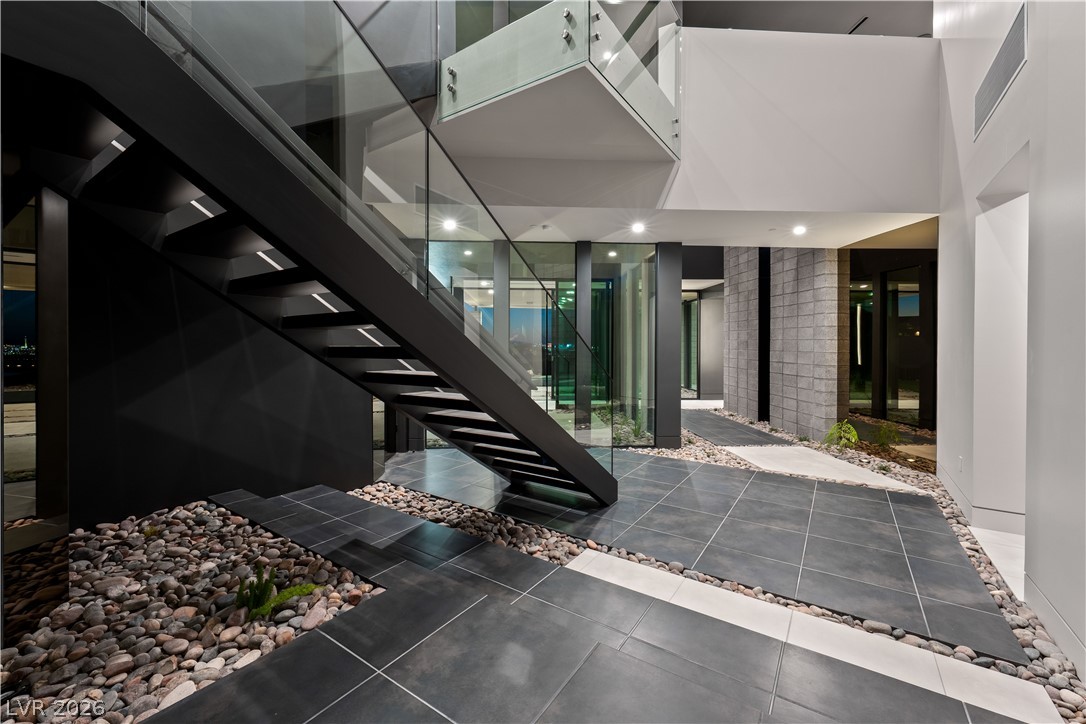 Modern entry foyer with a dramatic black staircase, glass railing, and river-rock floor beds.