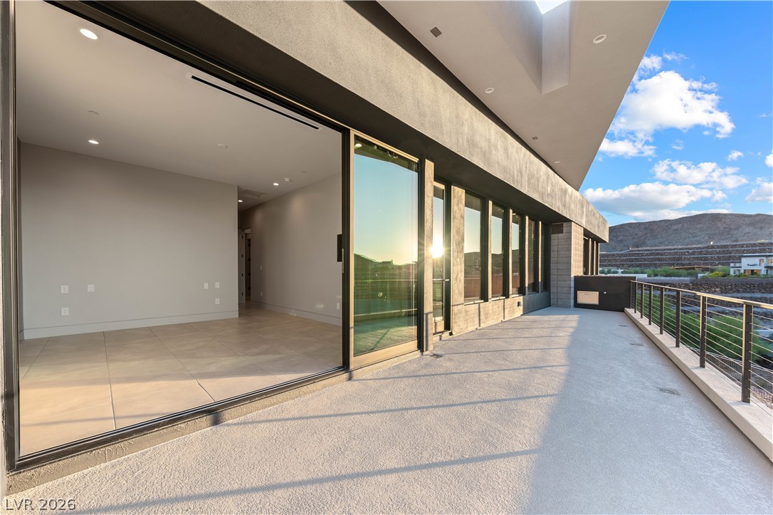 Modern home’s wide terrace with floor-to-ceiling glass doors, metal railing, and nearby hills.