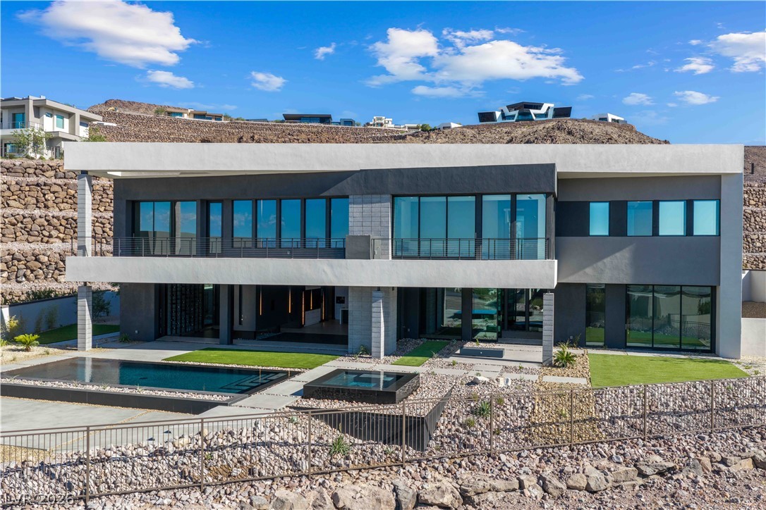 Modern two-story desert home with expansive glass facade, balcony, and swimming pool.