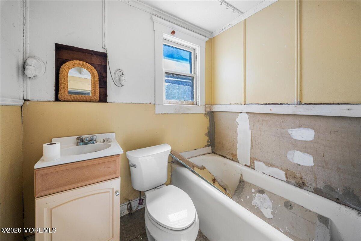 Bathroom with a small window, vanity, toilet, and partially stripped bathtub surround.