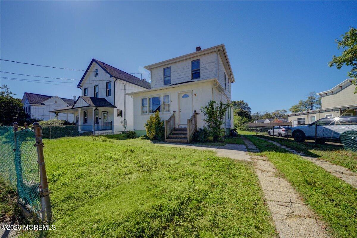 White two-story house with front steps, grassy yard, chain-link fence, and driveway.