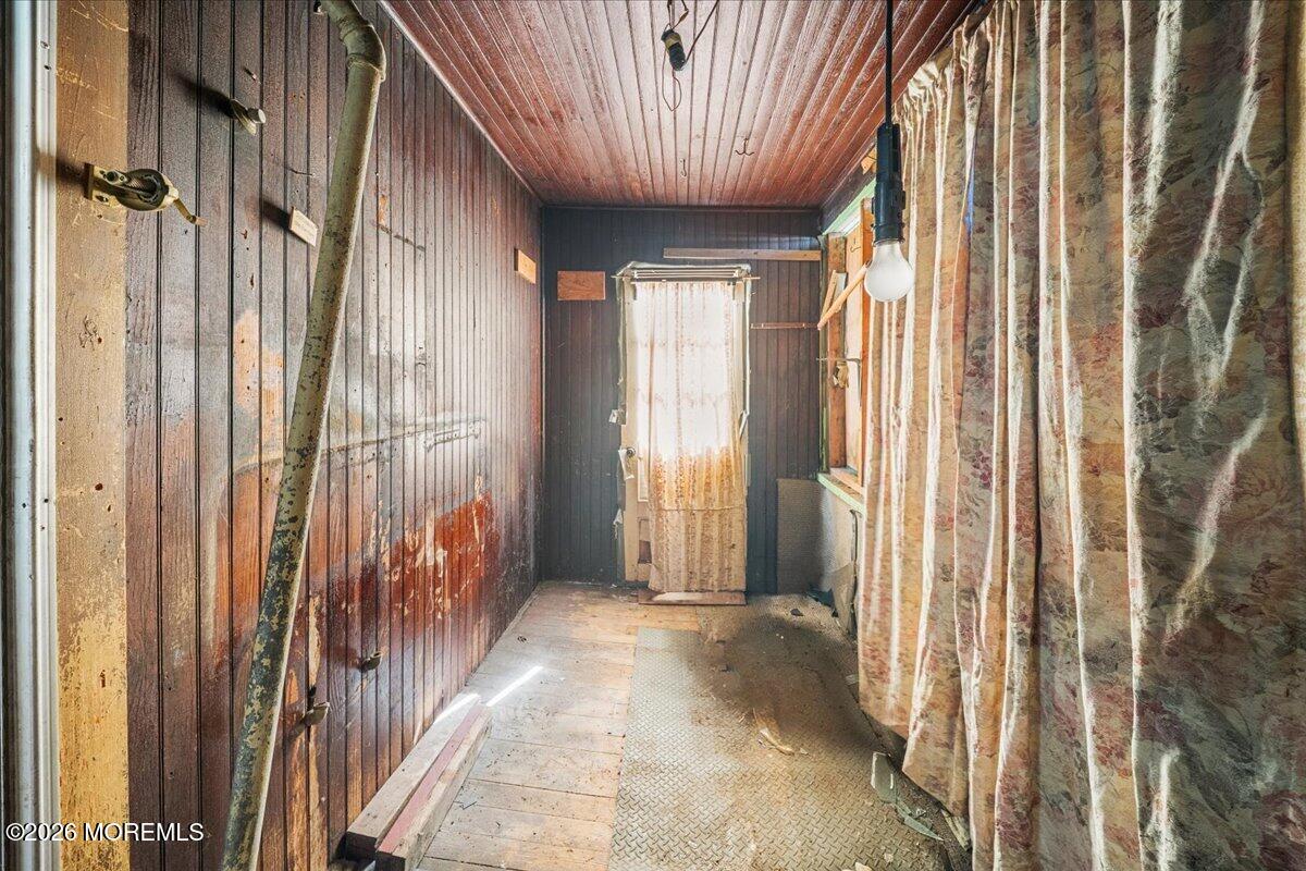 Narrow wood-paneled room with patterned curtains, a plank ceiling, and a bare, worn floor.