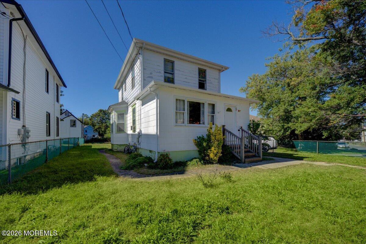 White two-story house with a small porch and wooden steps, seen from across the lawn.