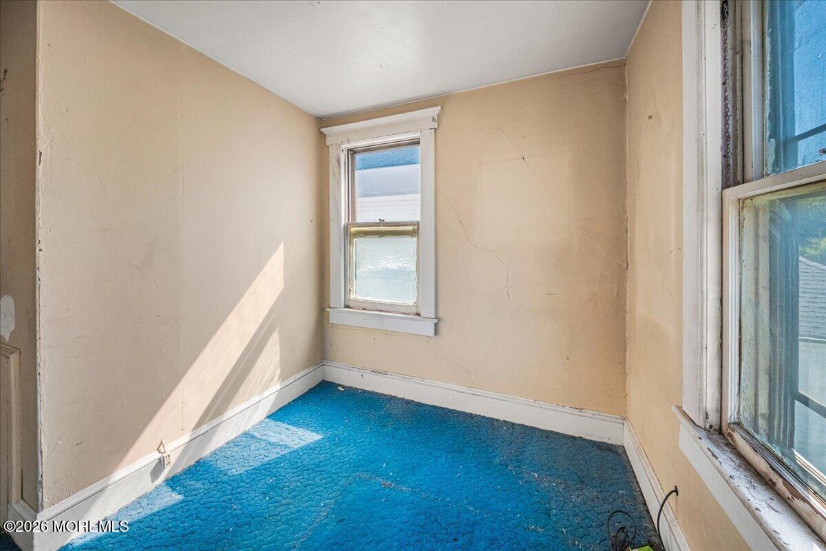 Empty room with bright blue carpet, worn beige walls, and two windows.