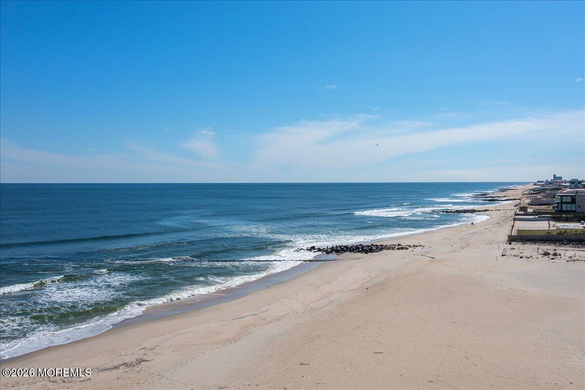 Sandy beach and ocean shoreline with beachfront homes in the distance.