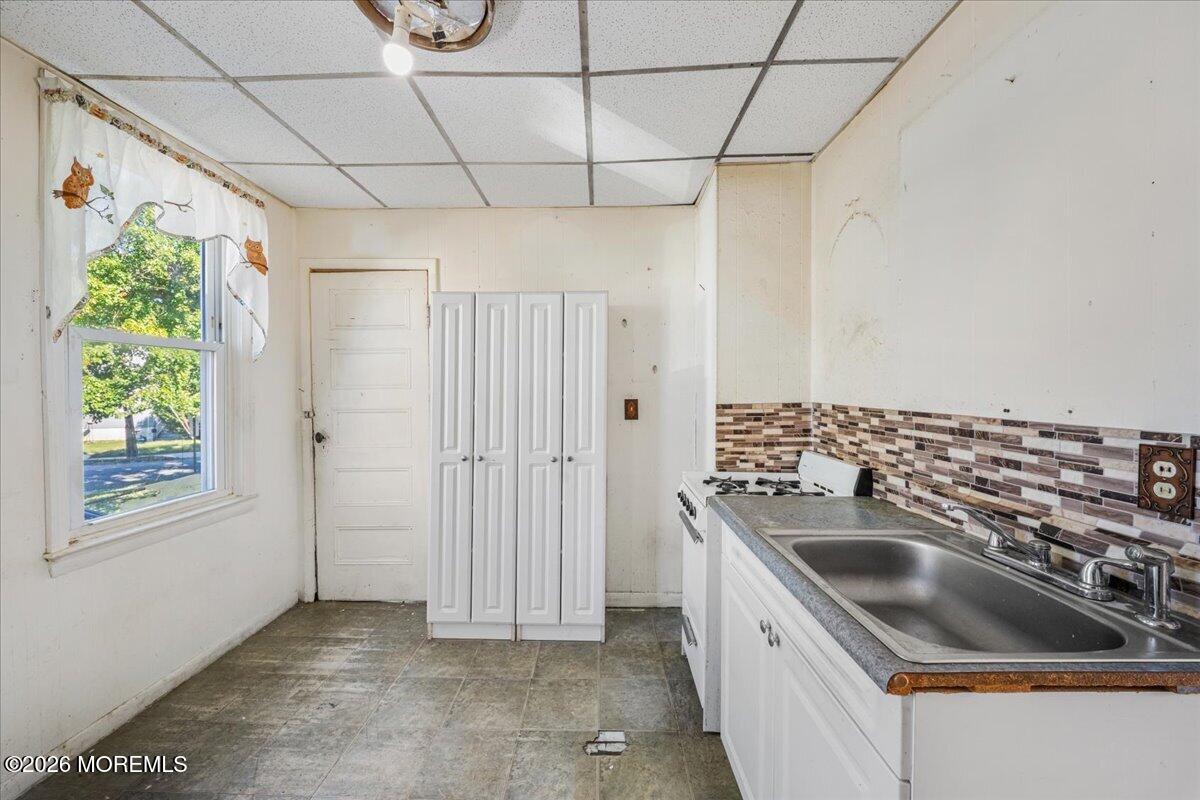 Kitchen with white cabinets, a gas stove, and a double-basin sink beneath a mosaic backsplash.