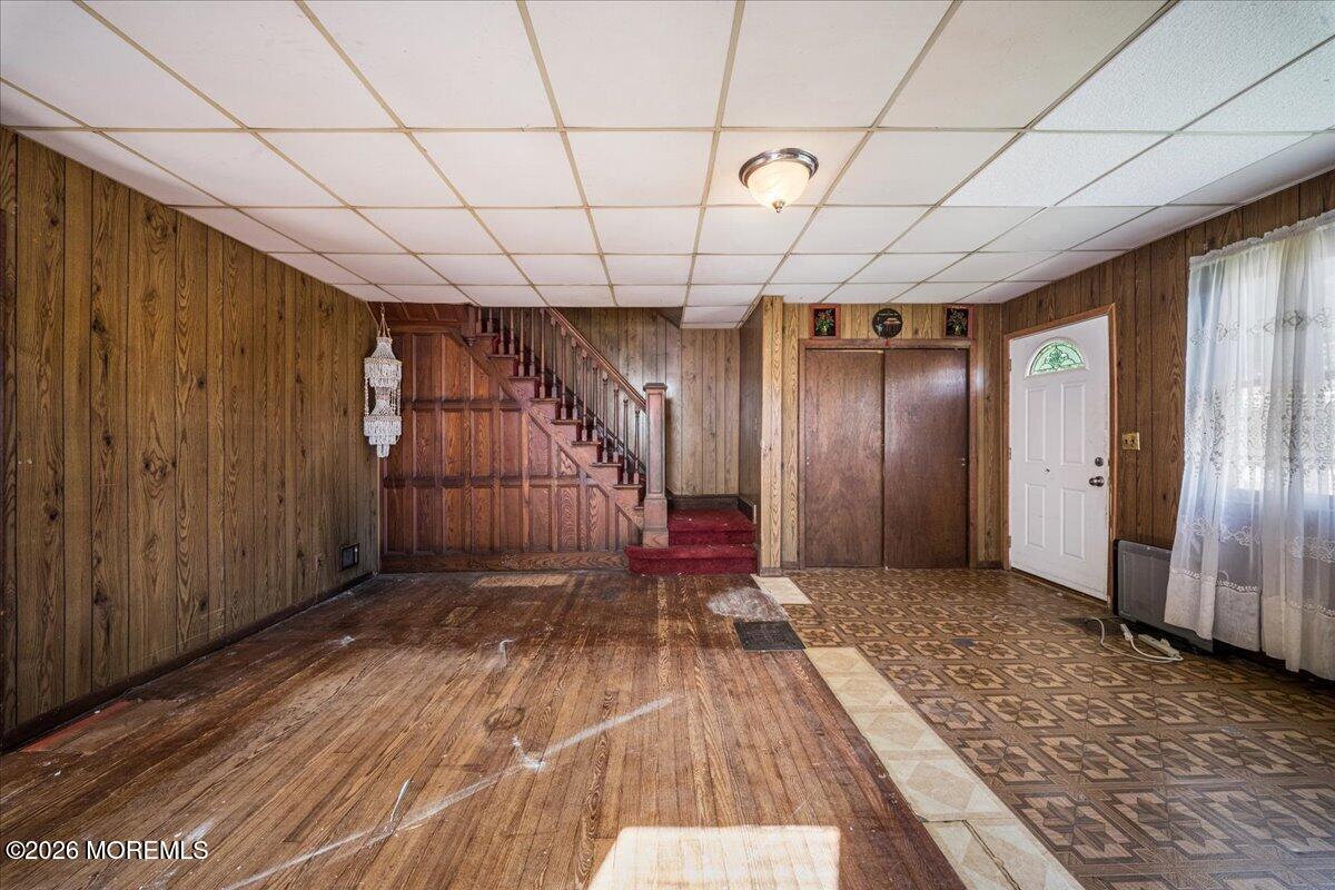 Vacant wood-paneled room with a staircase, white front door, and mixed wood and patterned flooring.
