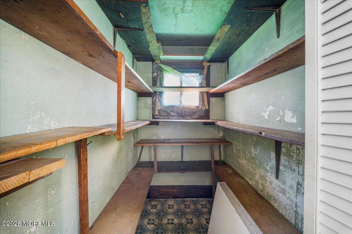 Narrow storage room with built-in wooden shelves, peeling green paint, and patterned floor tiles.