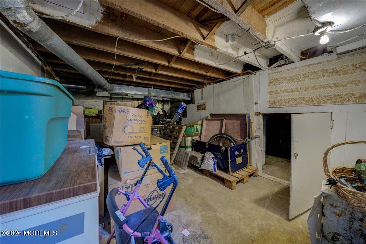 Unfinished basement storage area with exposed joists, ductwork, boxes, and a large blue bin.