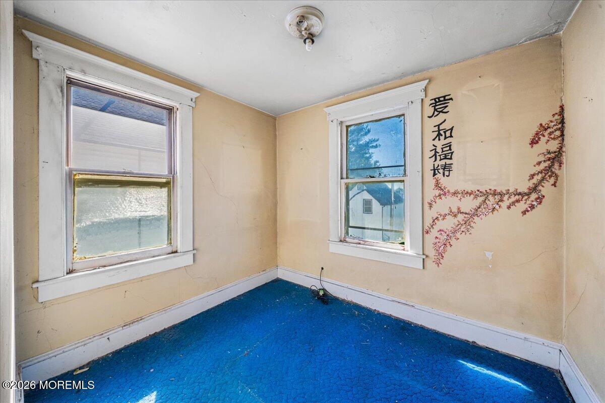 Empty room with worn blue carpet, beige walls, two windows, and Chinese calligraphy.