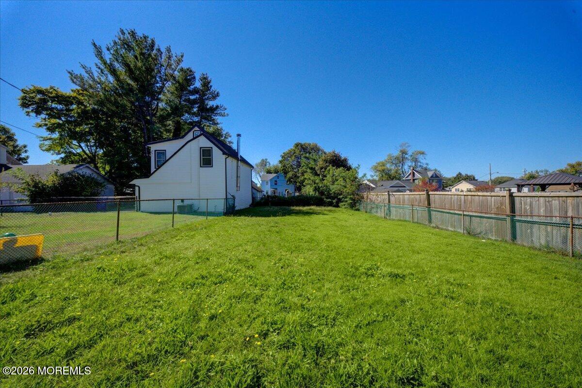 Spacious grassy backyard with fenced boundaries and a white house beyond.