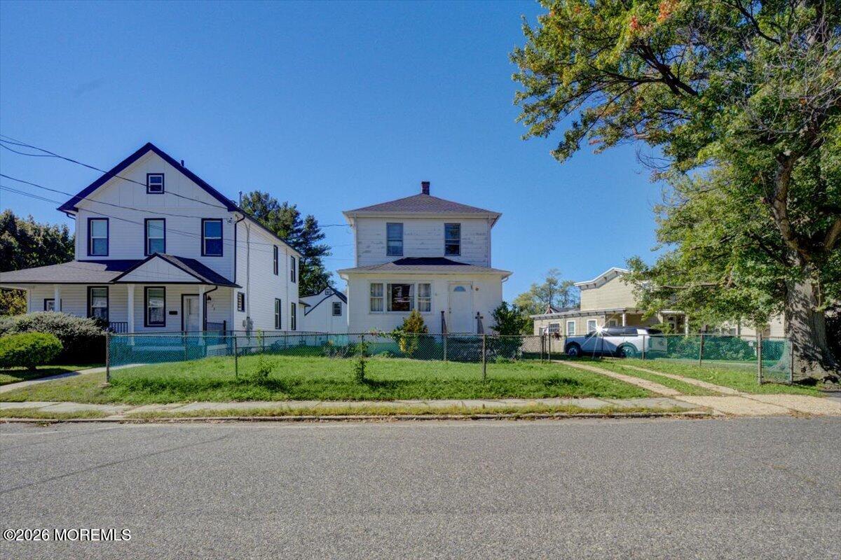 White two-story house with a fenced grassy yard, photographed from across the street.