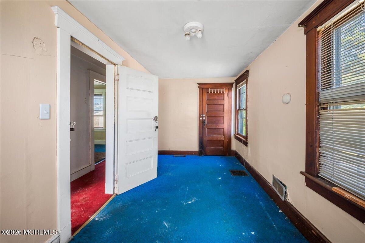 Entry hall with bright blue carpet, dark wood doors, and large windows with blinds.