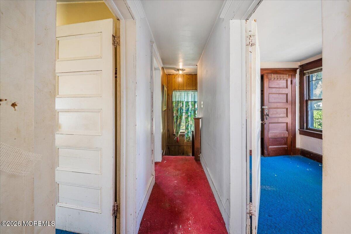 Narrow hallway with red carpet, white walls, and a wood-paneled end wall.