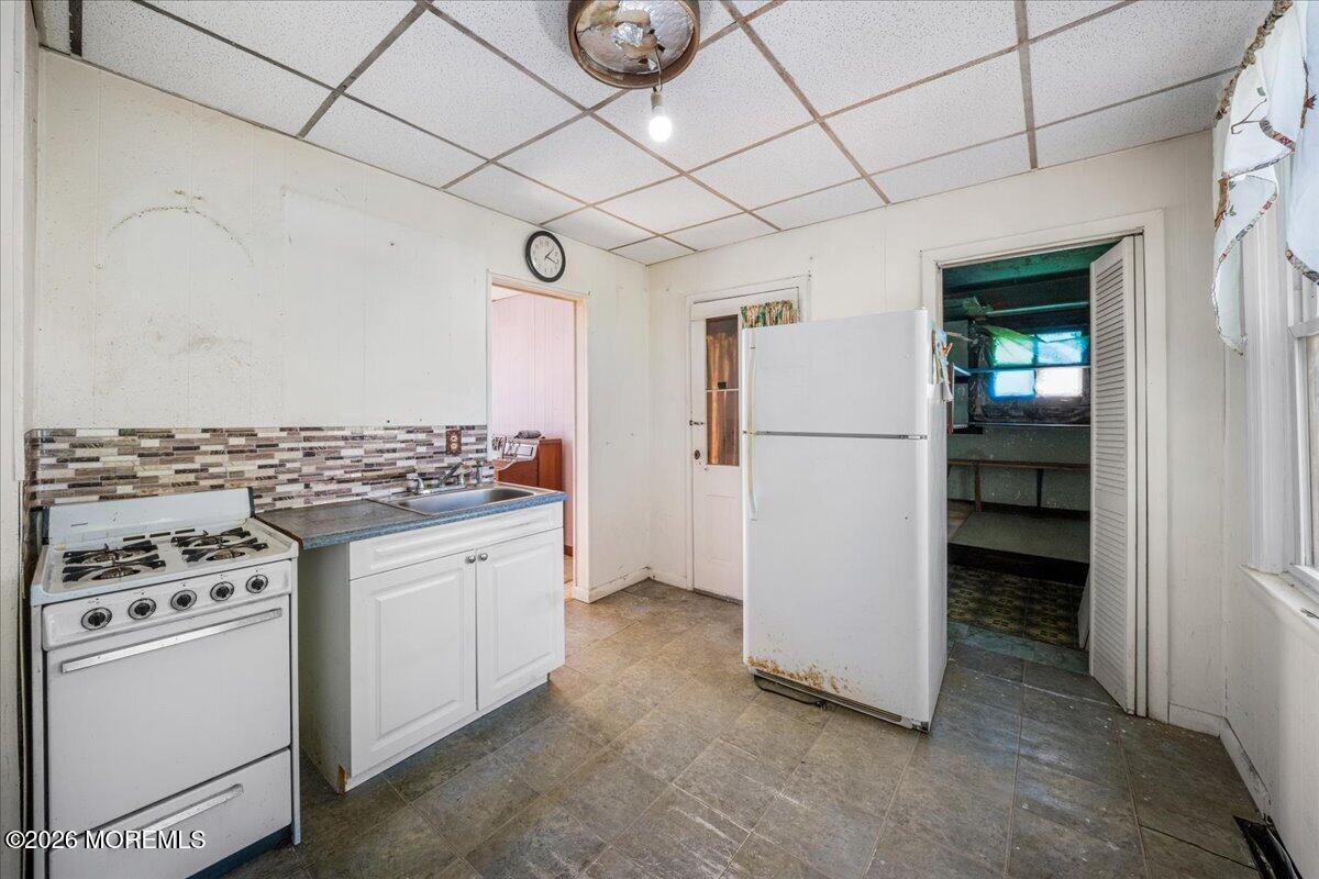 Kitchen with white stove and refrigerator, mosaic backsplash, and suspended ceiling.