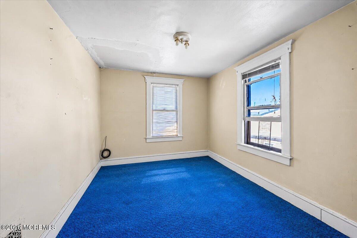 Empty room with bright blue carpet, two windows, and a damaged ceiling.