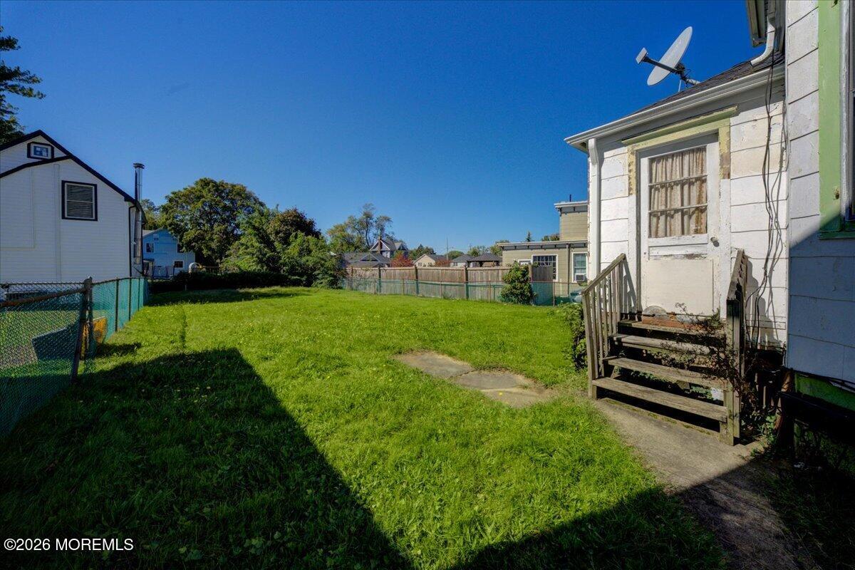 Fenced grassy backyard with a concrete walkway and wooden steps beside the house.
