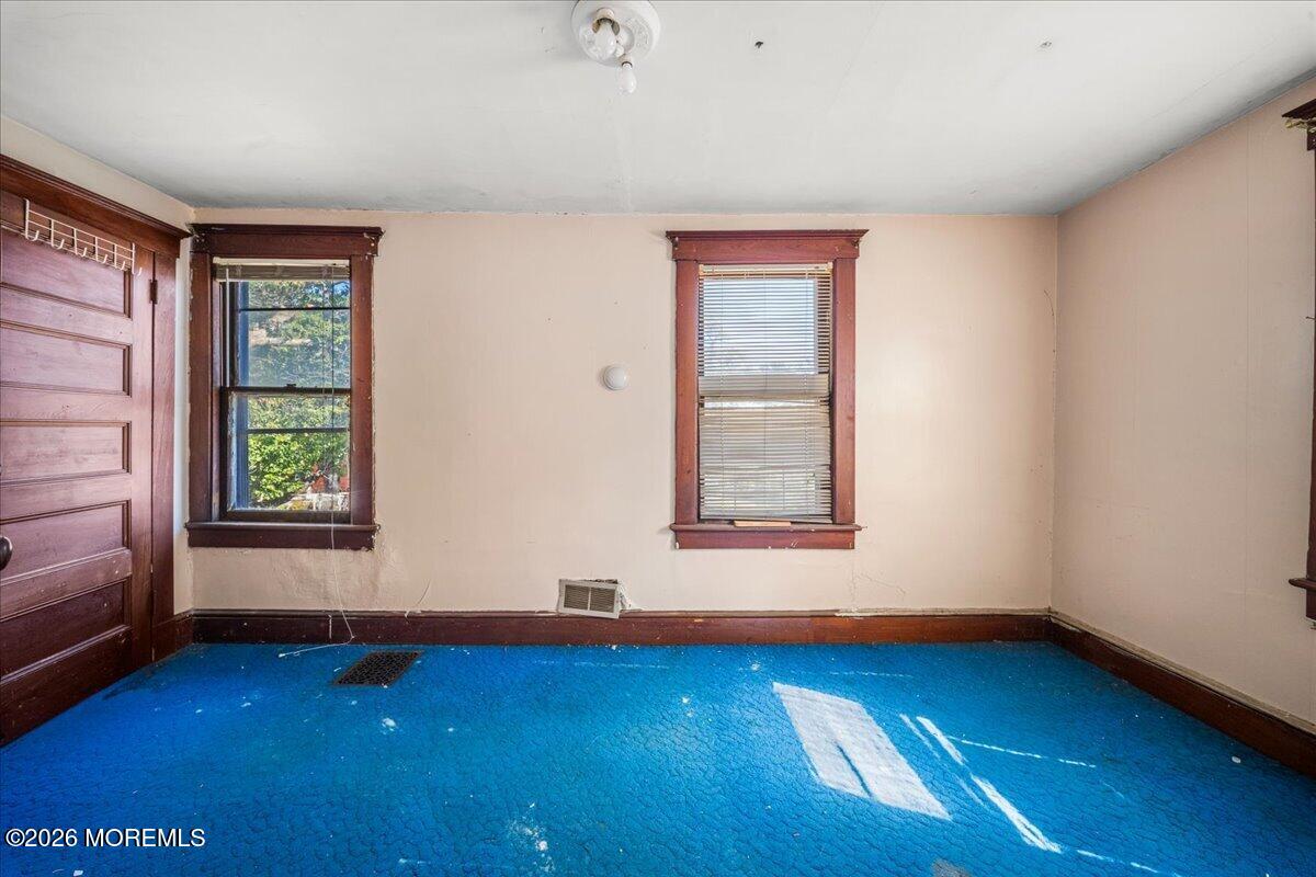Vacant room with bright blue carpet, two wood-trimmed windows, and a paneled door.