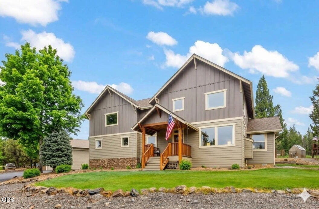 Two-story home with a covered wooden porch, American flag, and broad green lawn.