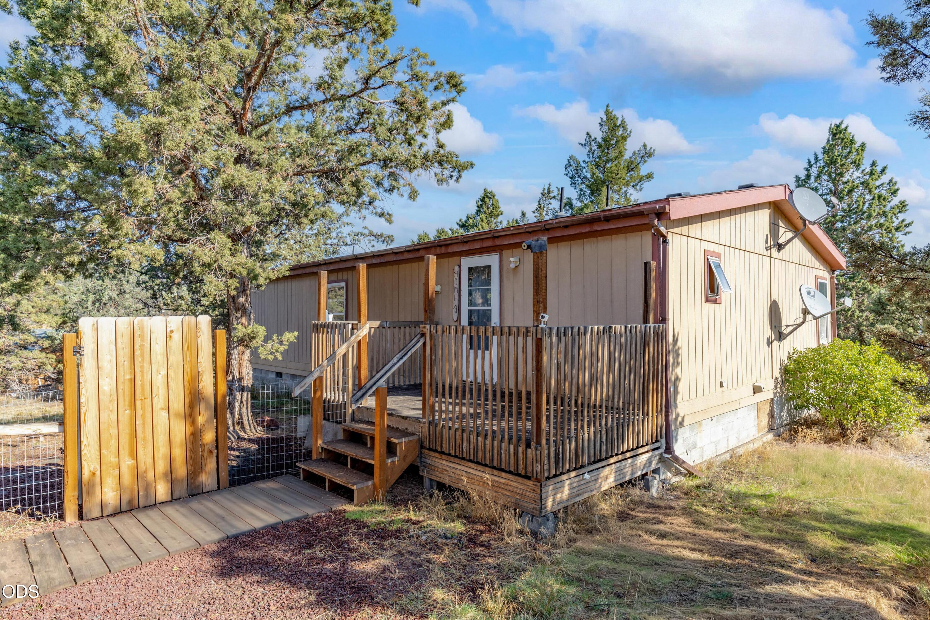 Tan home with a raised wooden porch and tall gate among pine trees.
