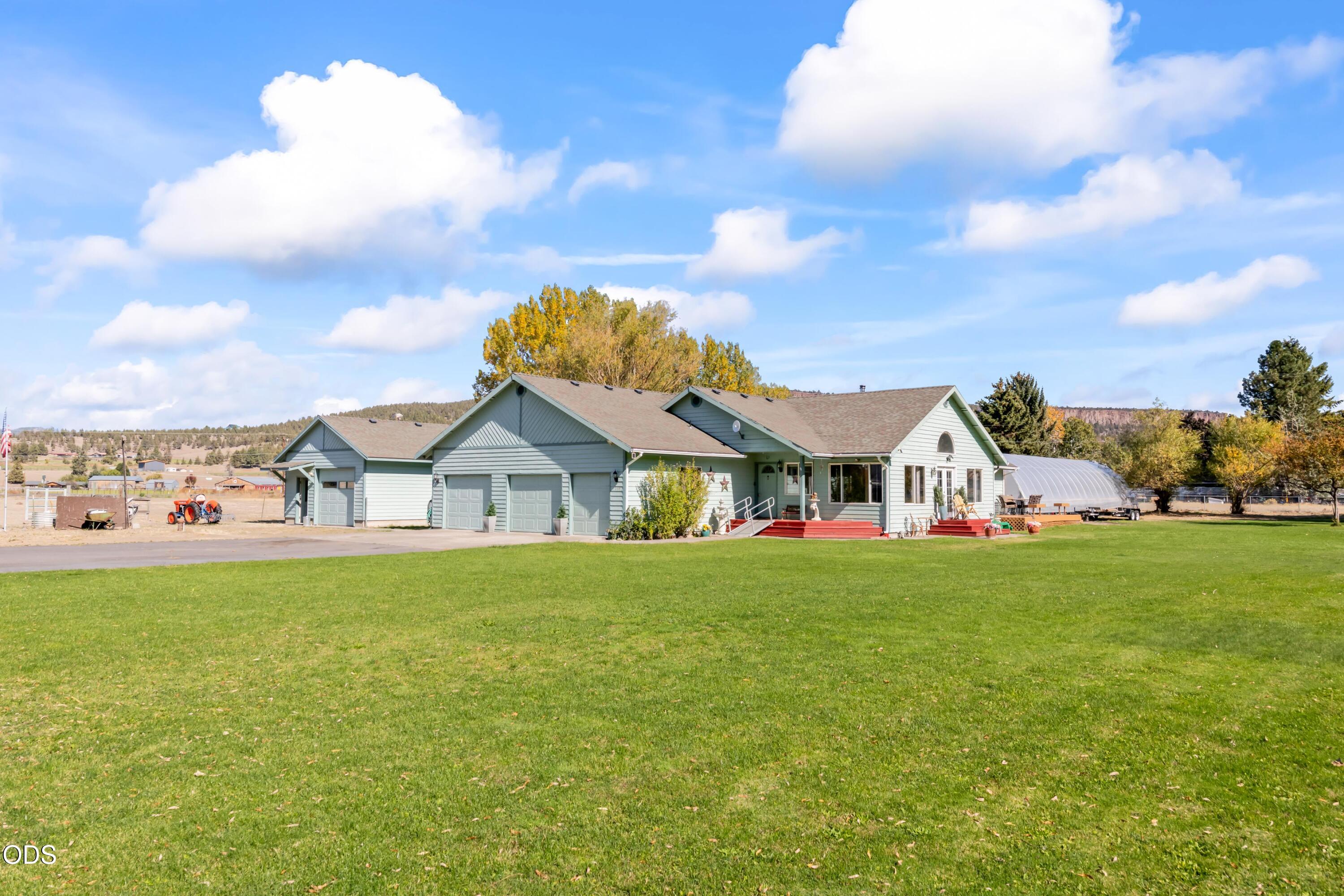 Ranch-style home with multiple garage bays, red entry steps, and a broad lawn beside a greenhouse.