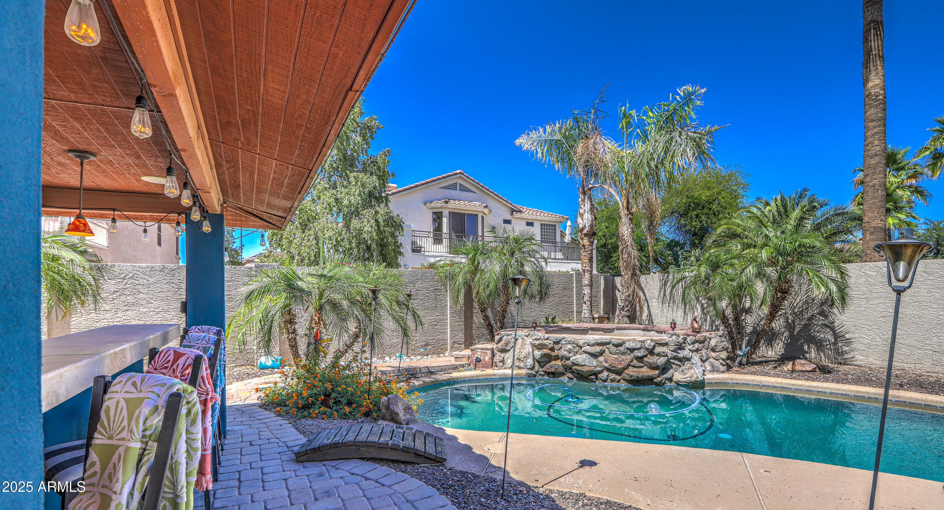 Backyard pool with a raised rock waterfall, palm trees, and covered patio seating.