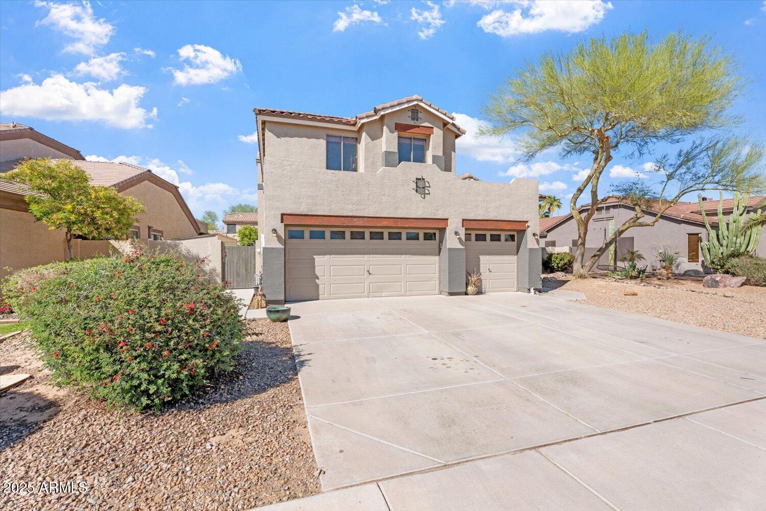 Two-story stucco home with a two-car garage, wide driveway, and desert landscaping.
