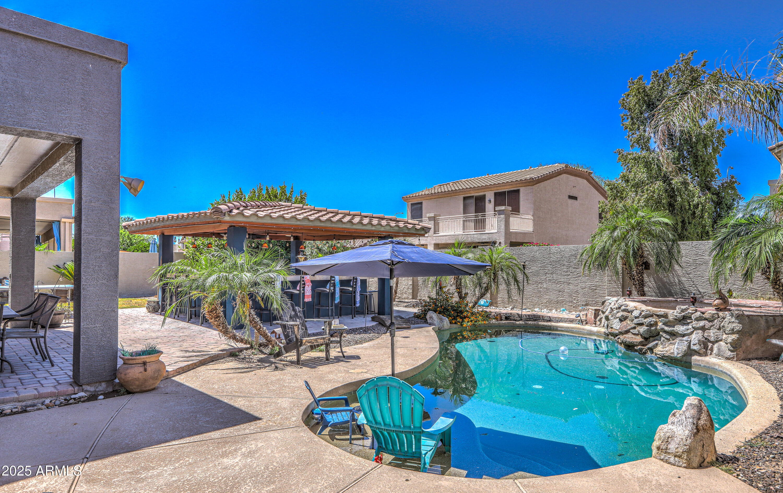 Backyard pool with a rock waterfall, covered bar, and palm trees.