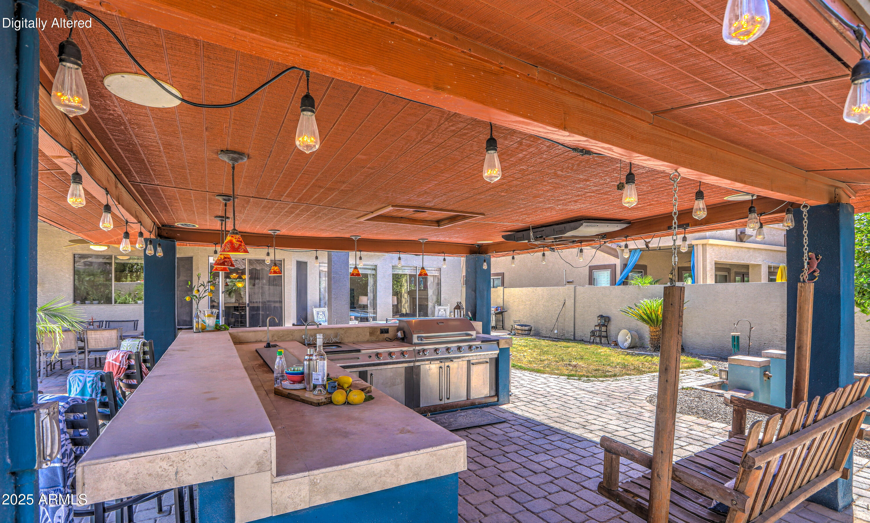 Covered outdoor kitchen with a built-in grill, broad stone counters, hanging lights, and a wooden porch swing.