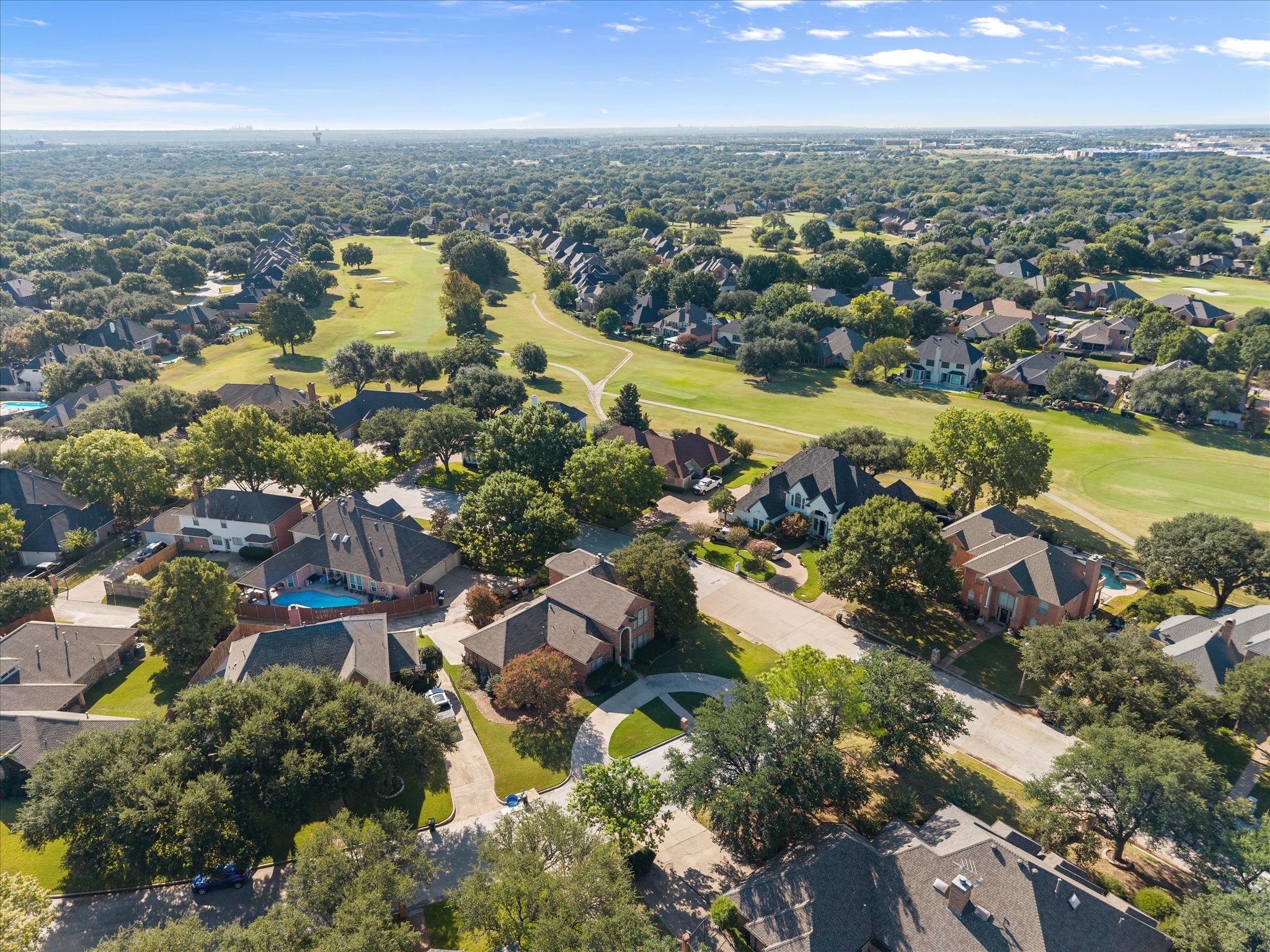 Aerial view of homes bordering a golf course, with mature trees and winding paths.