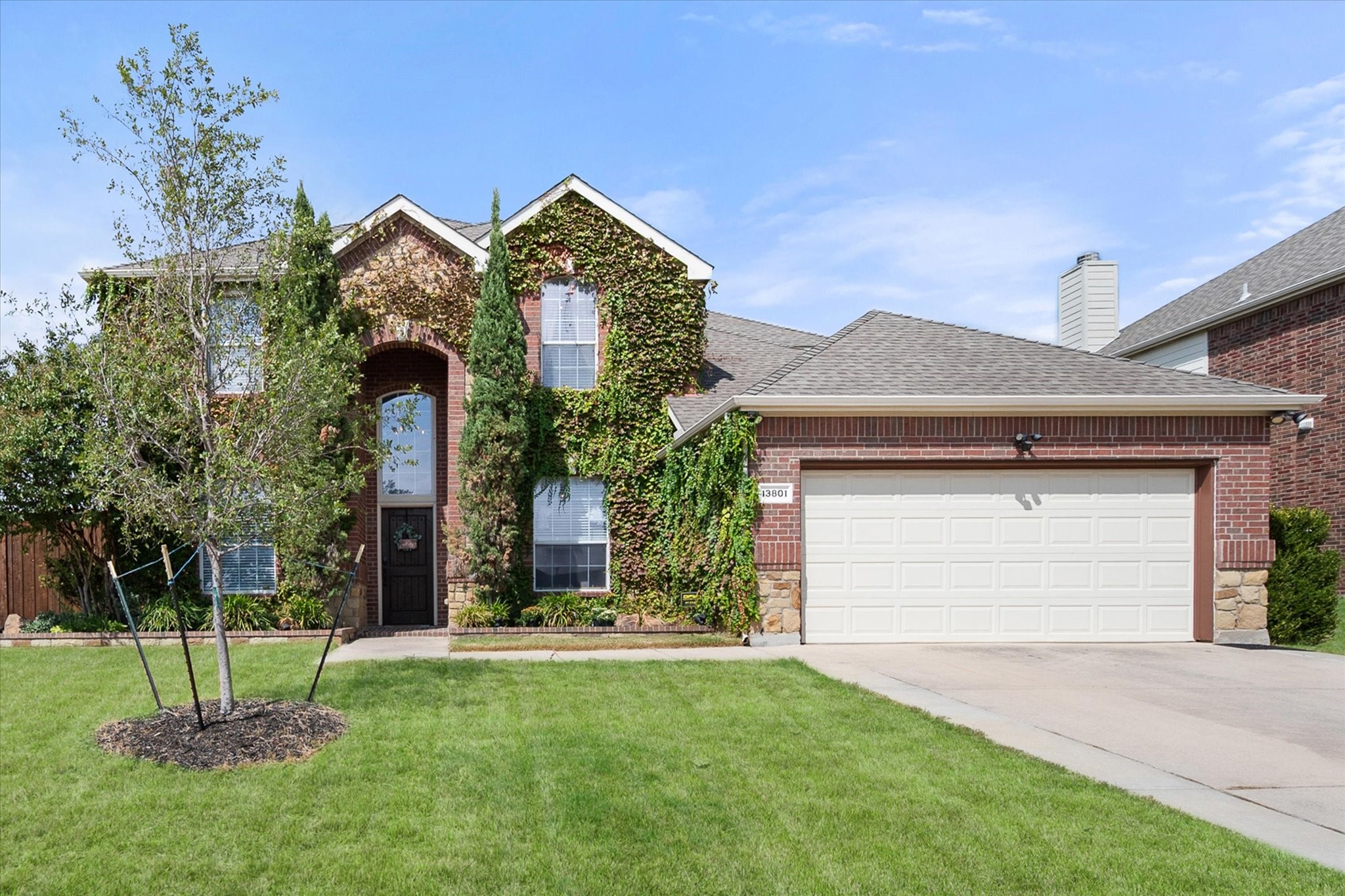 Two-story brick home with ivy-covered facade, white garage door, and broad front lawn.