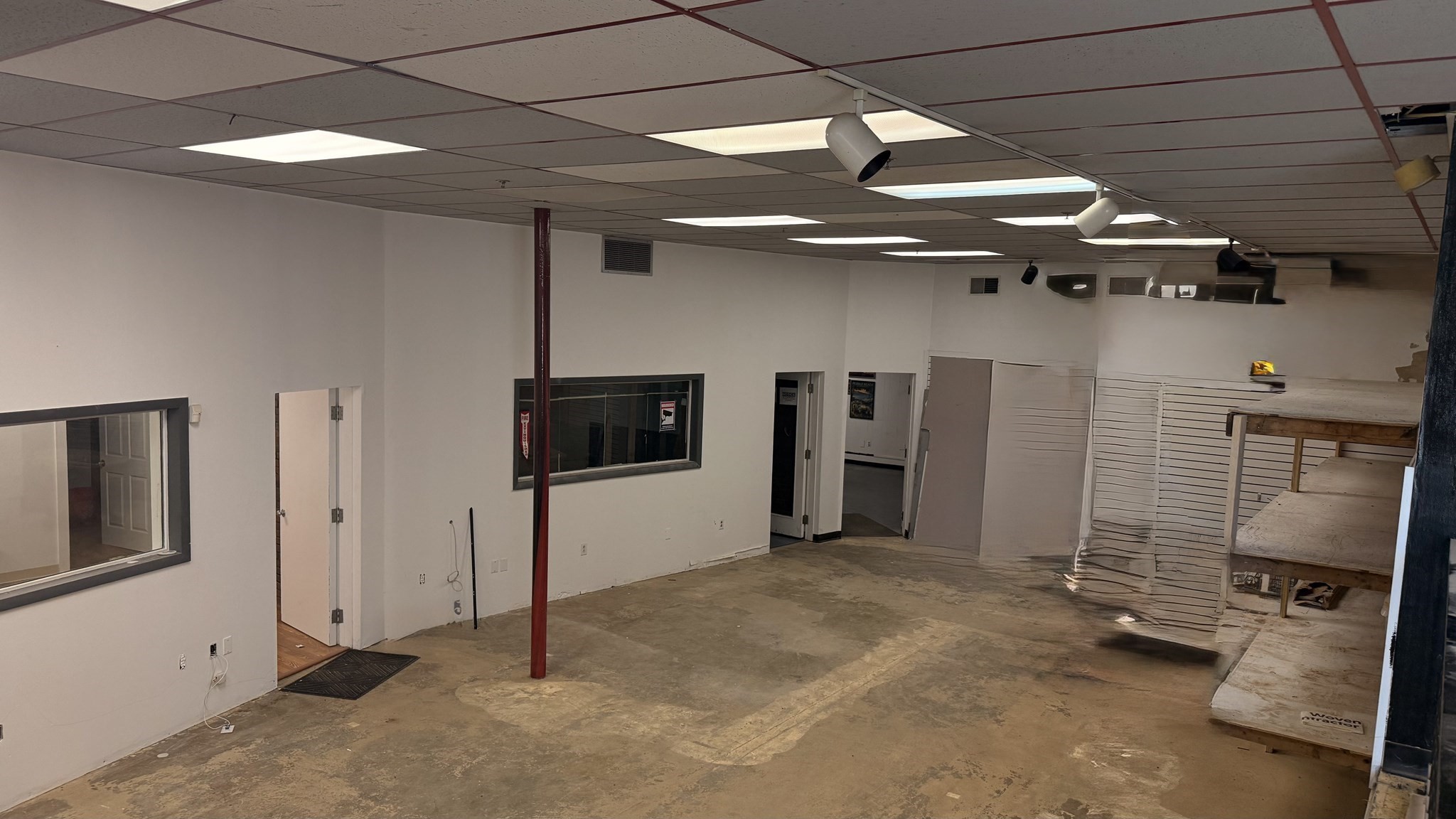 Vacant commercial interior with a concrete floor, partitioned rooms, and a raised wooden platform.