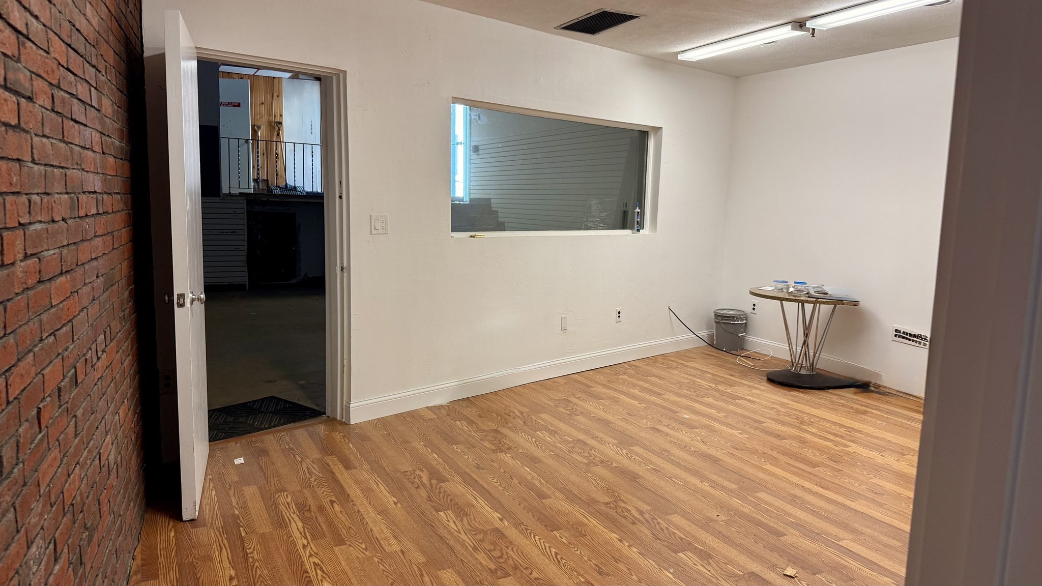 Empty room with a wood plank floor, exposed brick wall, and large interior window.